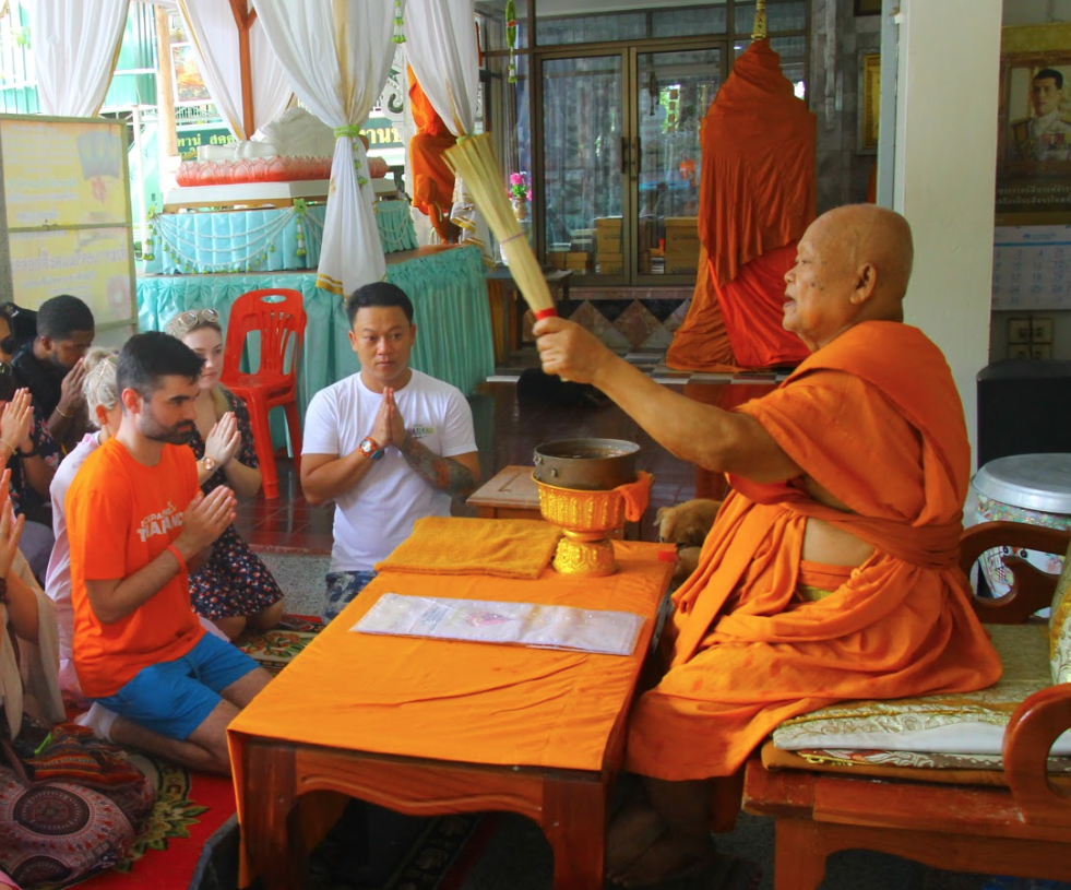 An elderly Buddhist monk performs a blessing for kneeling visitors in a temple in Thailand.