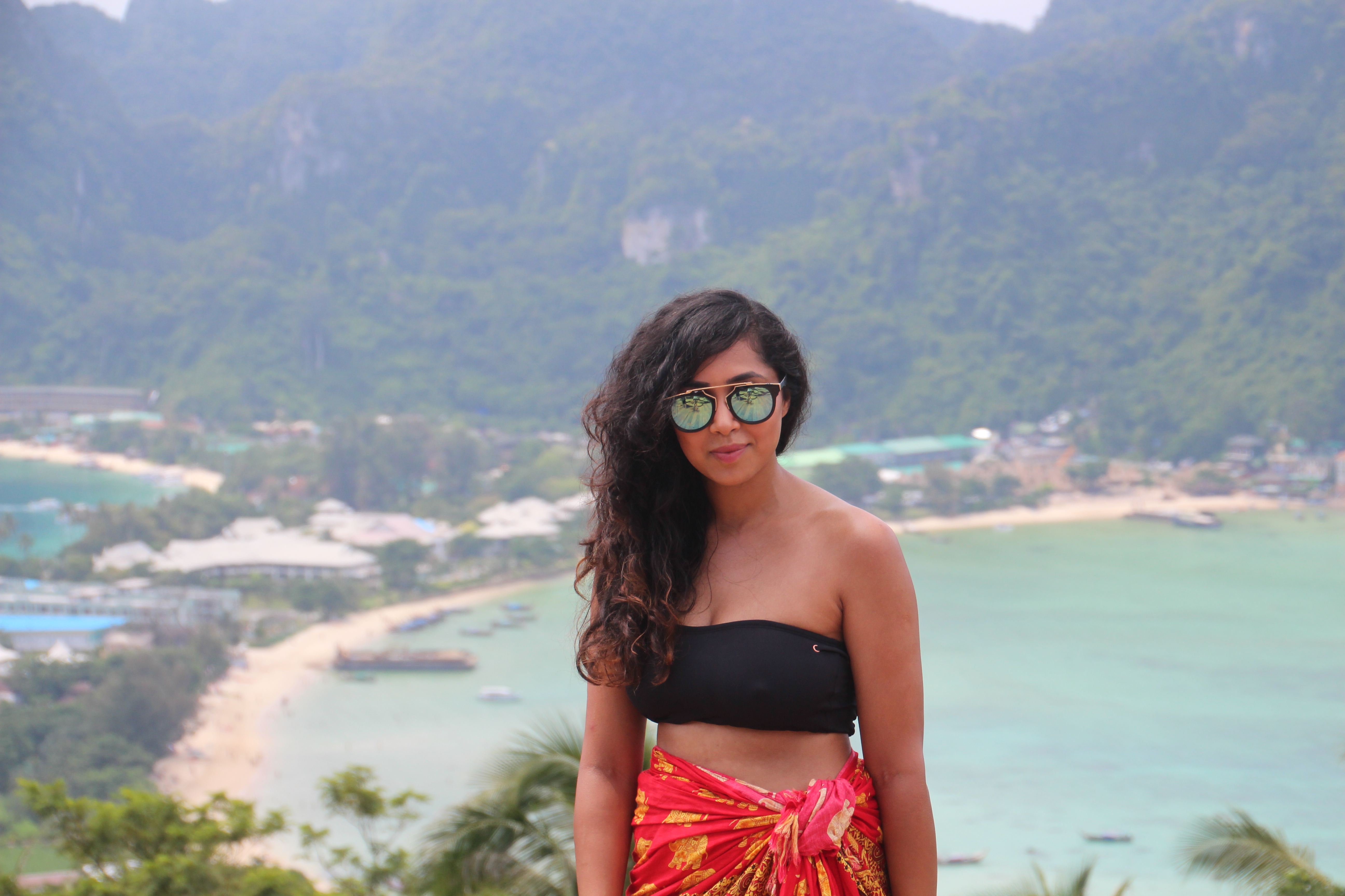 Woman in sunglasses and a sarong poses overlooking a beautiful tropical bay in Thailand.