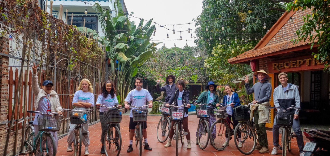 A group of smiling friends pose with their bicycles in a lush courtyard in Vietnam.
