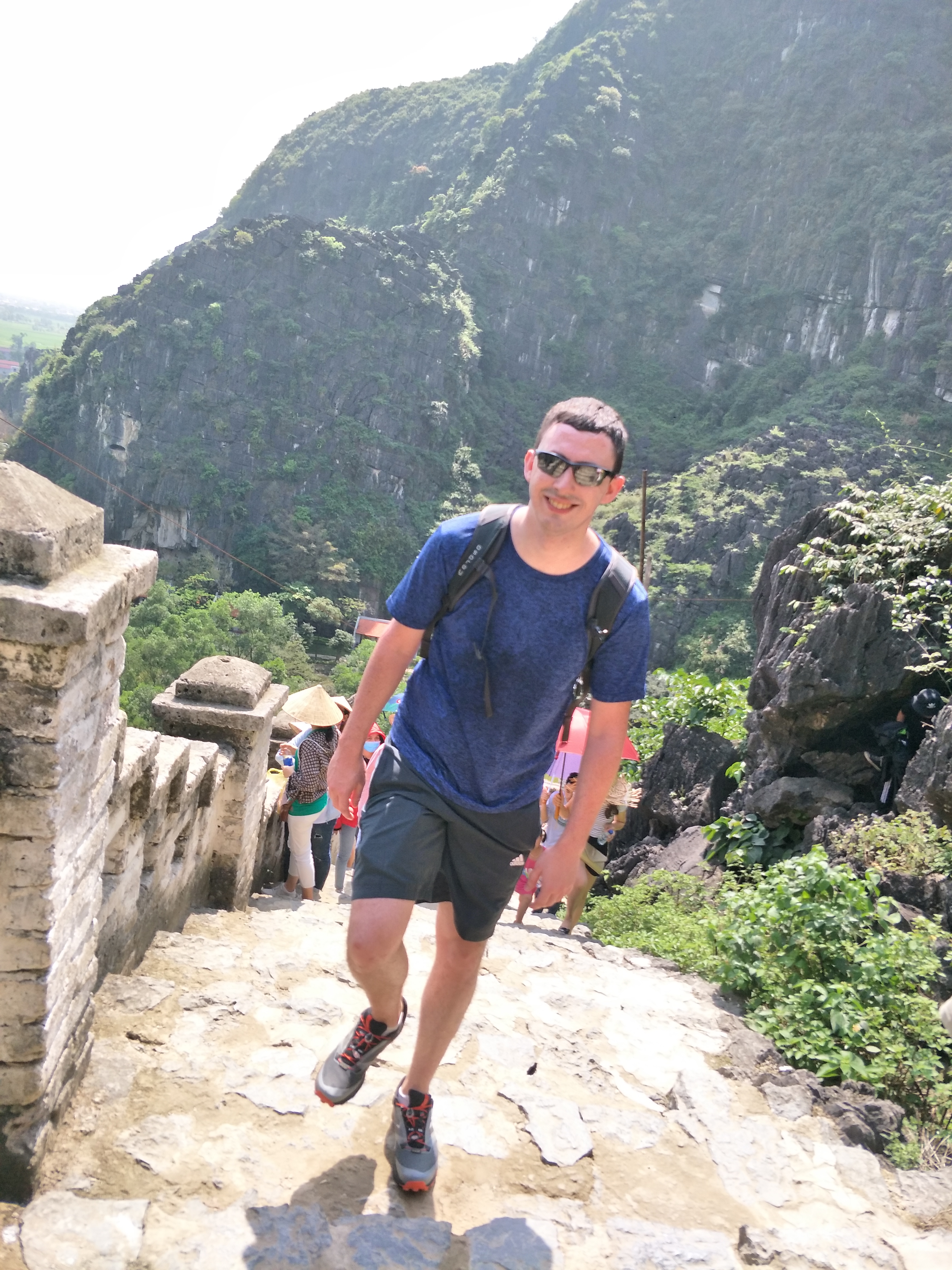A smiling man hikes up ancient stone steps in Vietnam's scenic karst mountains.