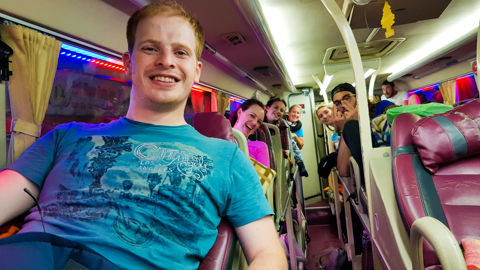 A happy man smiles at the camera inside a colorful sleeper bus in Vietnam.