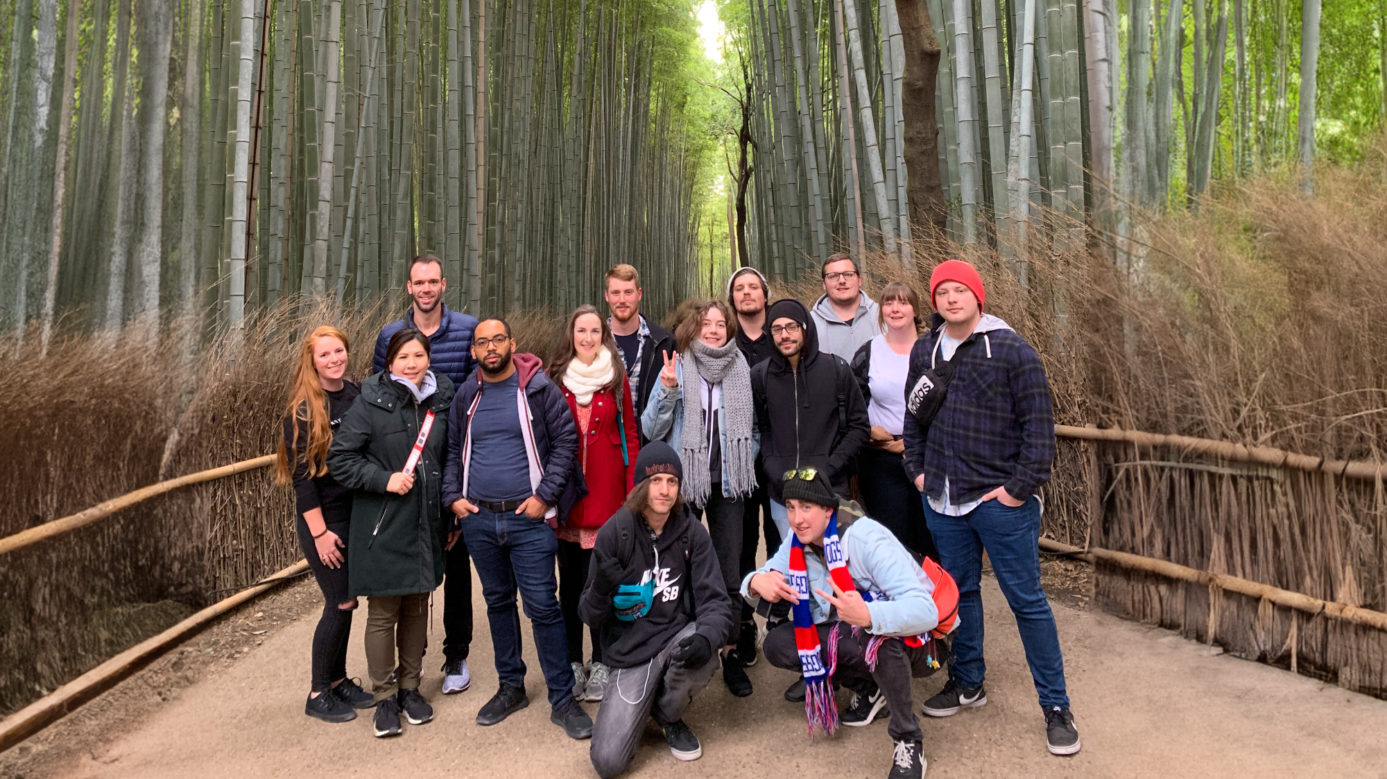A happy group of diverse backpackers posing on a path in the dense Arashiyama bamboo forest.