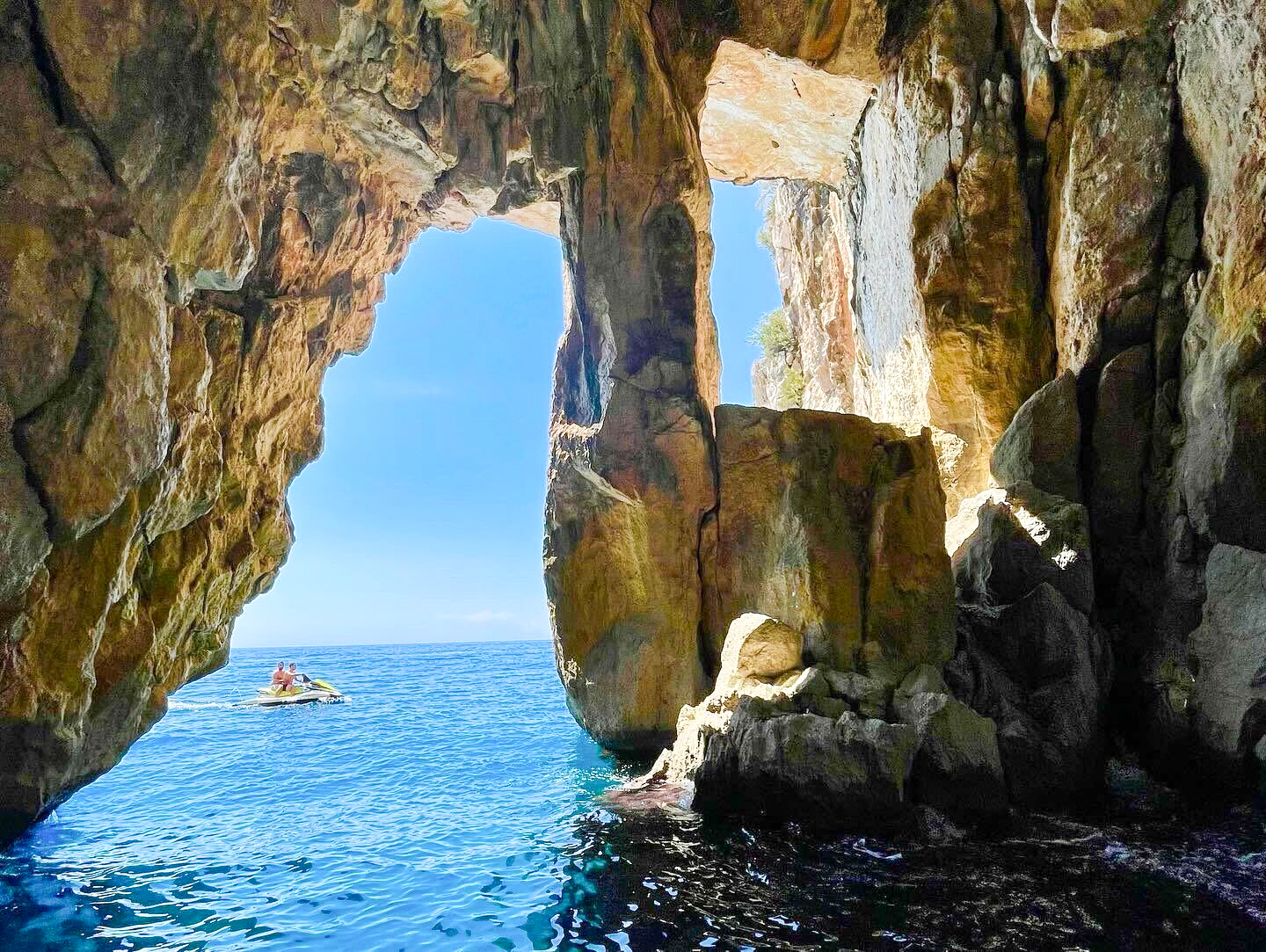 A boat heading out through a rock arch in a sea cave on the coast near Himarë