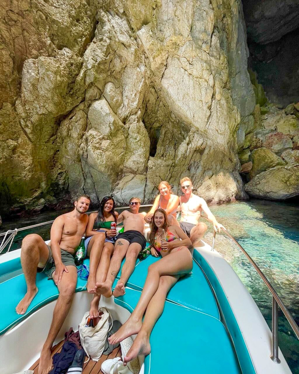 Six travellers relaxing on the bow of a boat beside the cliffs of the Himarë coast