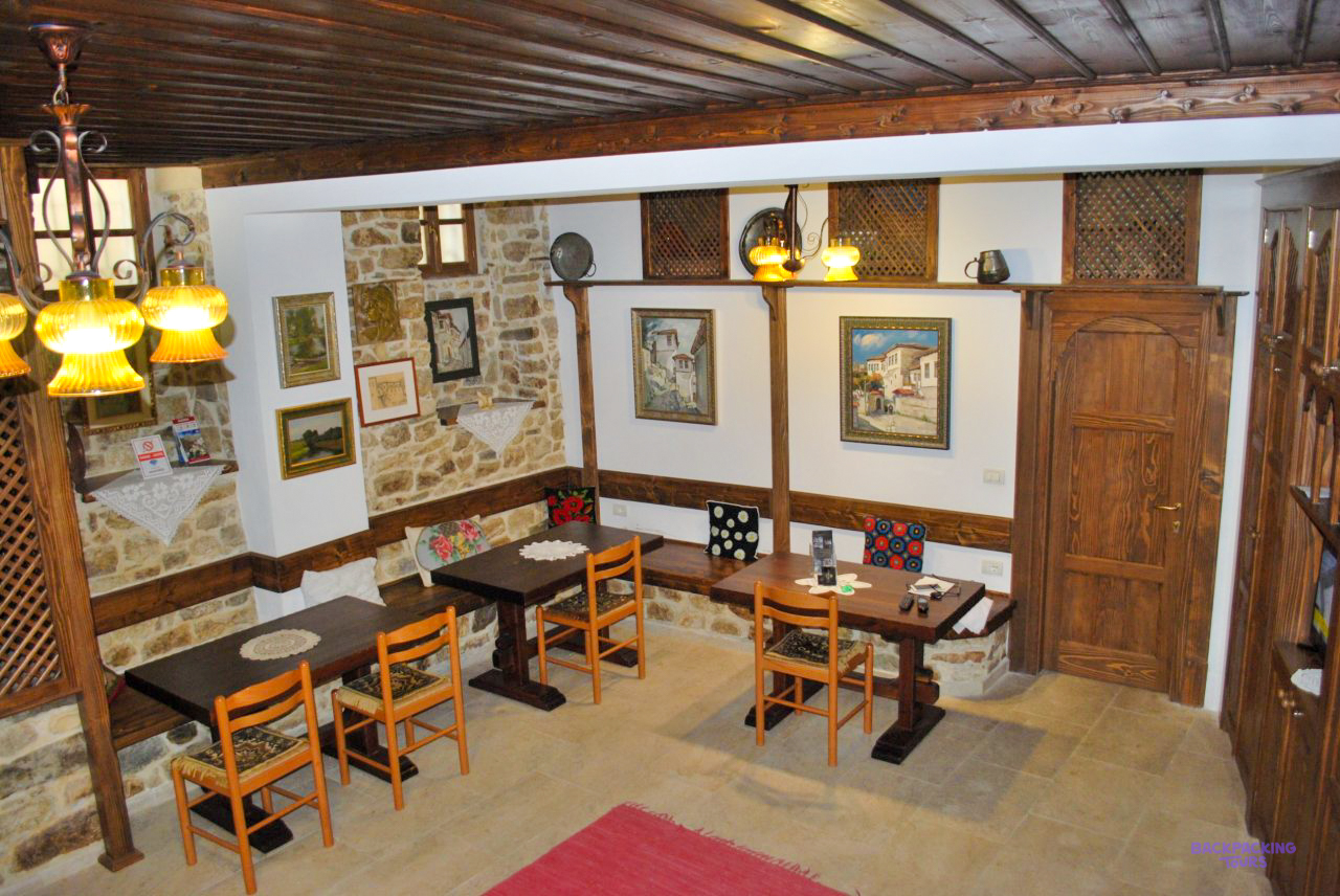The dining room of the guesthouse in Berat, with stone walls, wooden tables and hanging lamps