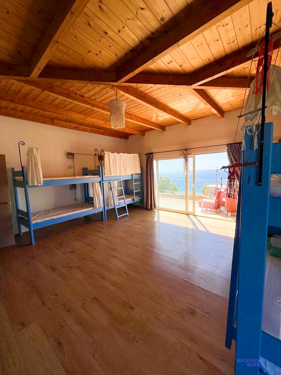 A bright dorm room with a wooden ceiling and a balcony at the hostel in Himarë