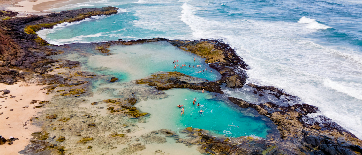 People swim and relax in clear turquoise Champagne Pools on K'gari (Fraser Island) by the ocean.
