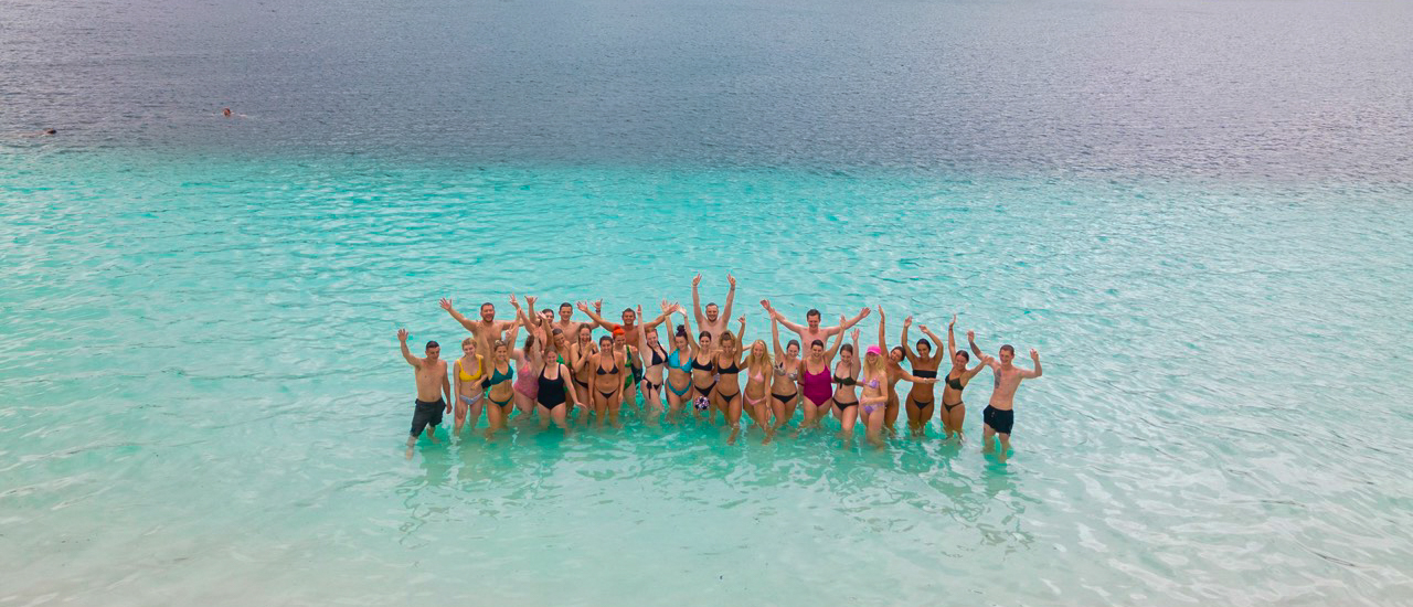 A large group of joyful backpackers celebrating in the crystal-clear turquoise waters of Lake McKenzie.