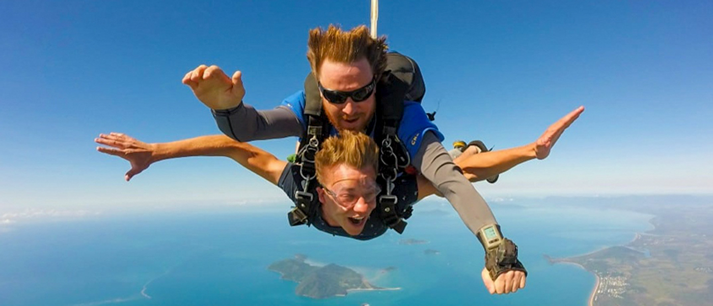 Two people tandem skydiving high above the beautiful blue ocean and coastline near Mission Beach, Australia.