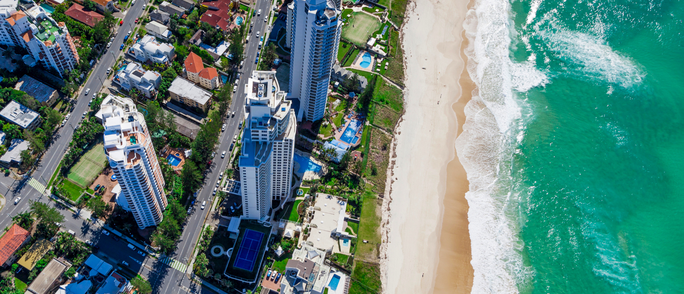 Aerial view of Surfers Paradise showing high-rise buildings, a long sandy beach, and turquoise ocean.