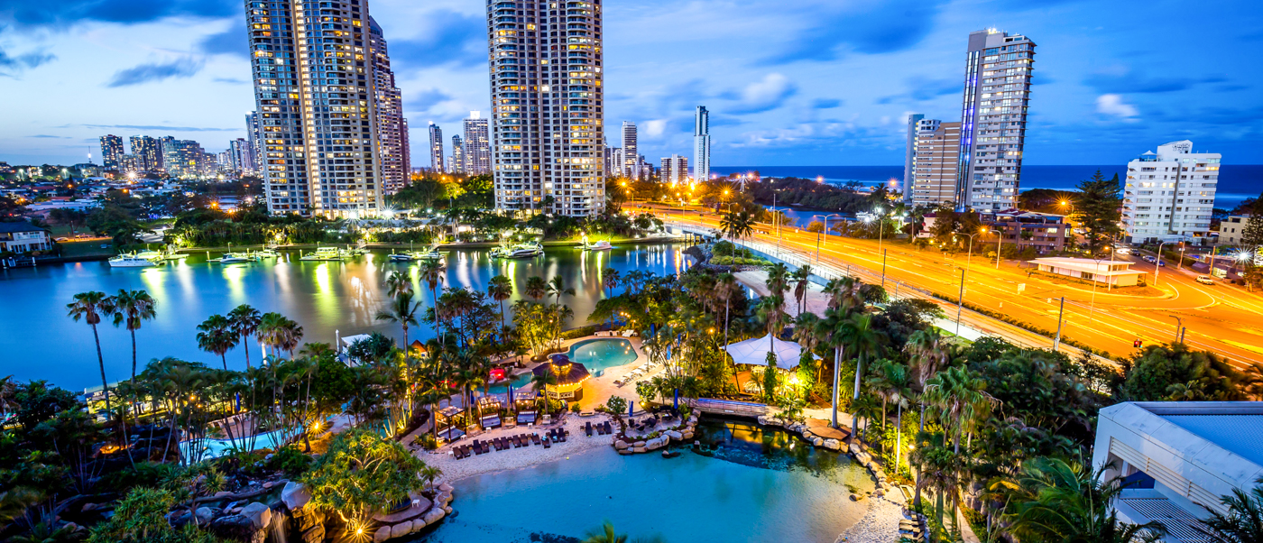 Vibrant Surfers Paradise cityscape at twilight, with illuminated high-rises, resort pools, and ocean views.