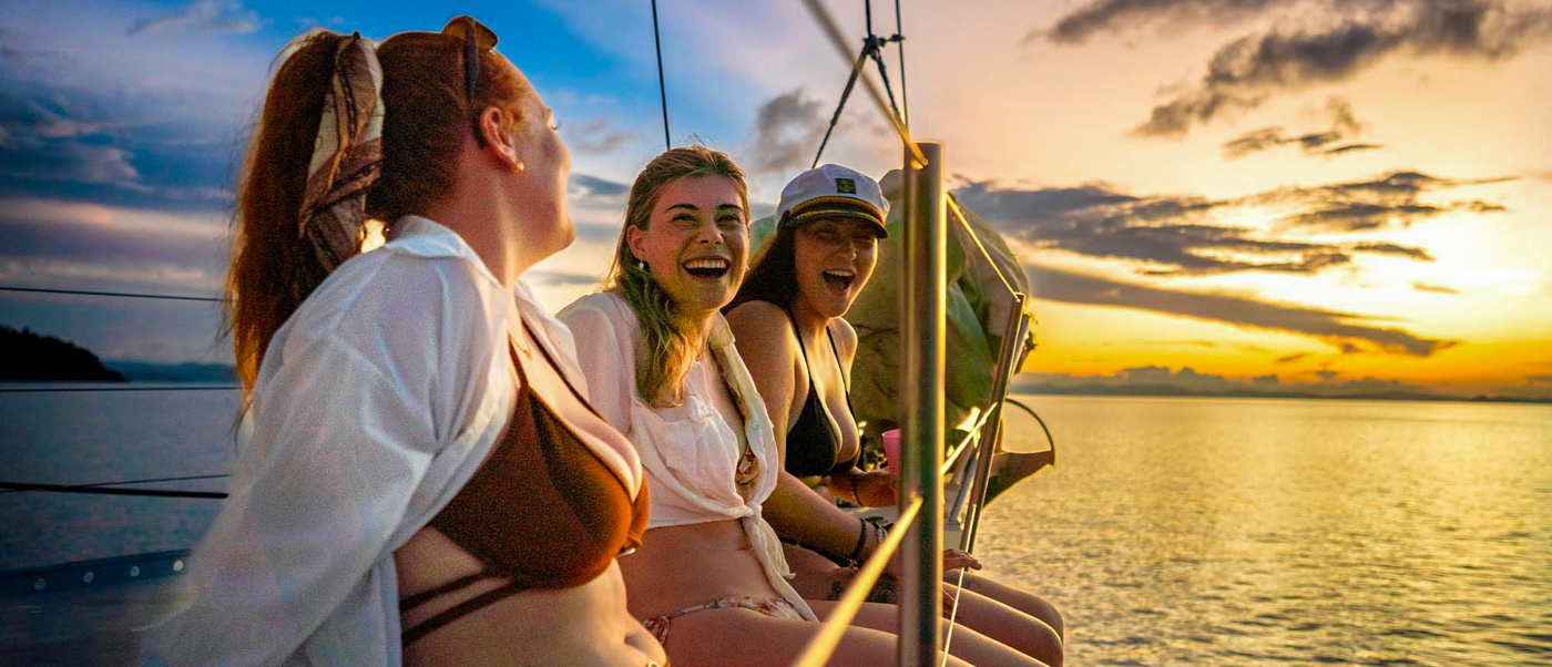 Joyful women on a boat watching a vibrant sunset over the Whitsundays islands.