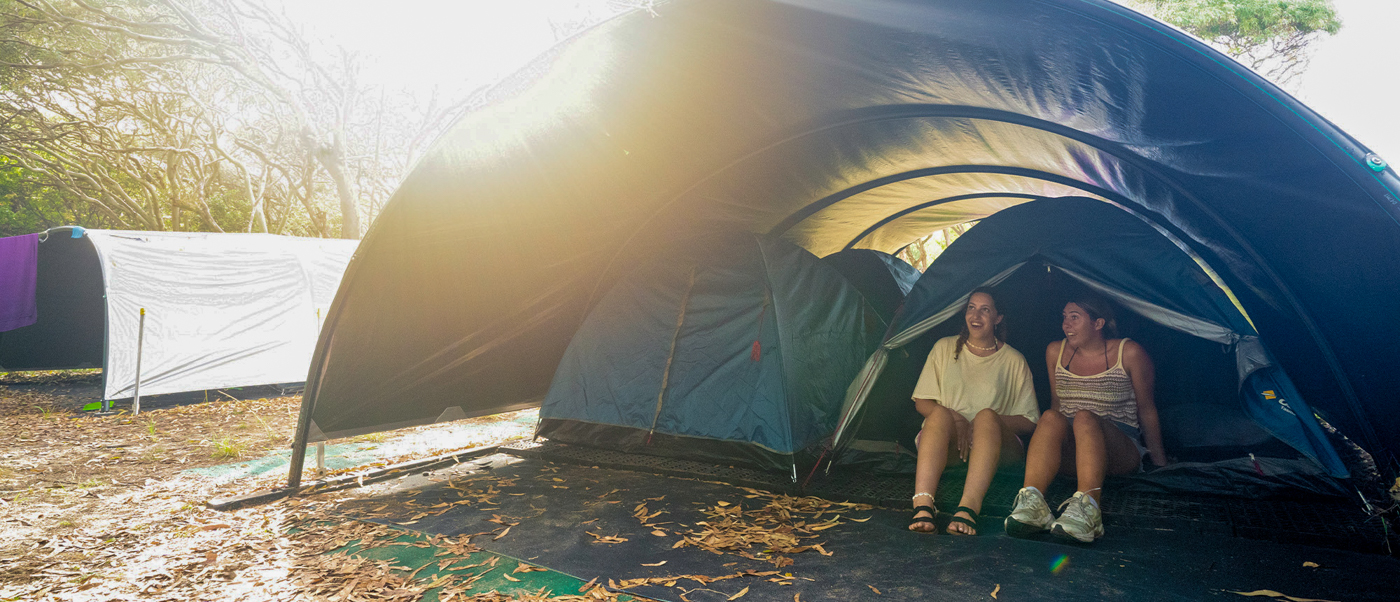Two young women relax inside a large tent at a sunny K'gari (Fraser Island) campsite.