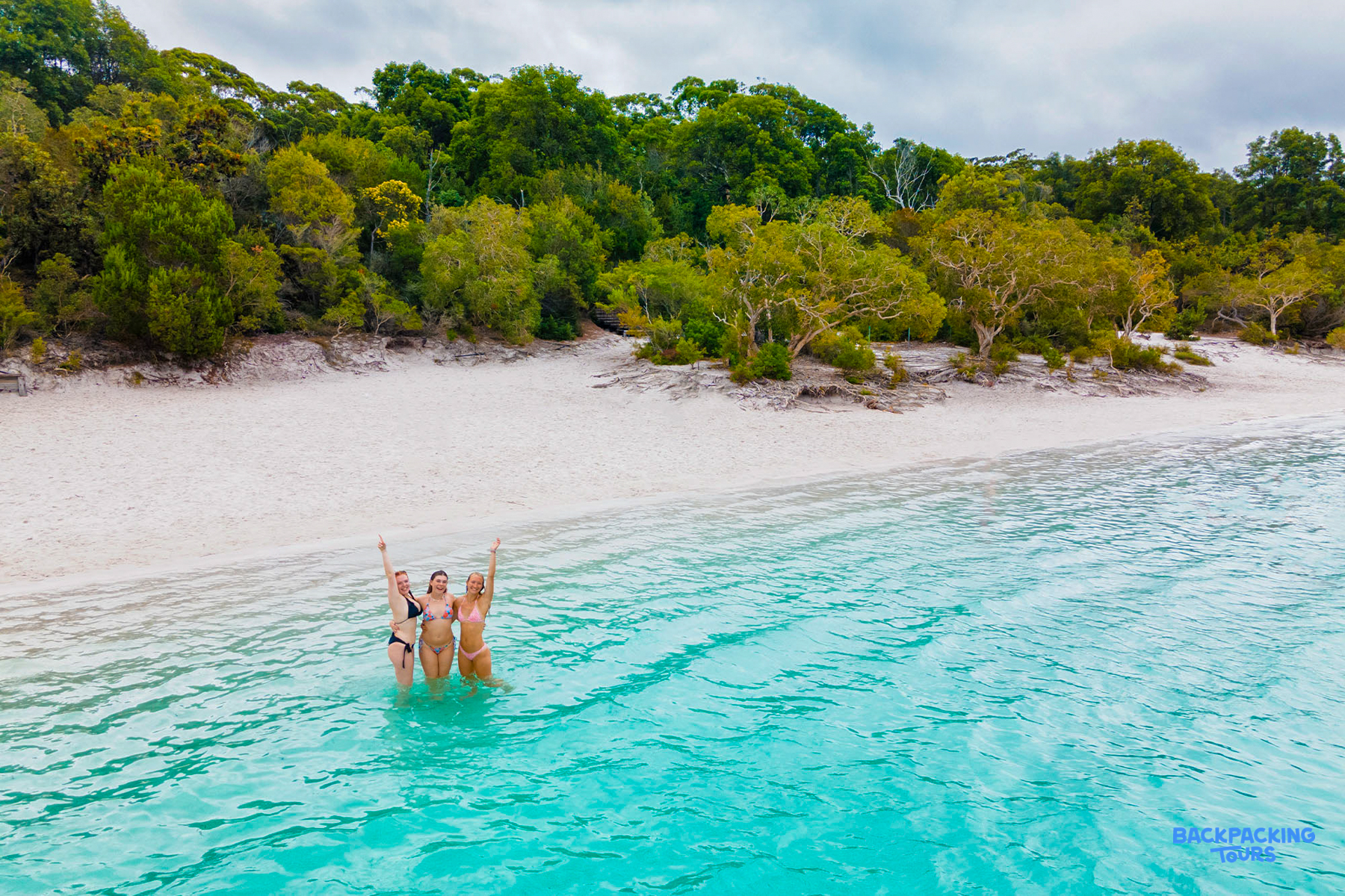 Three happy women celebrating in the crystal-clear turquoise waters of Lake Mackenzie, Fraser Island.