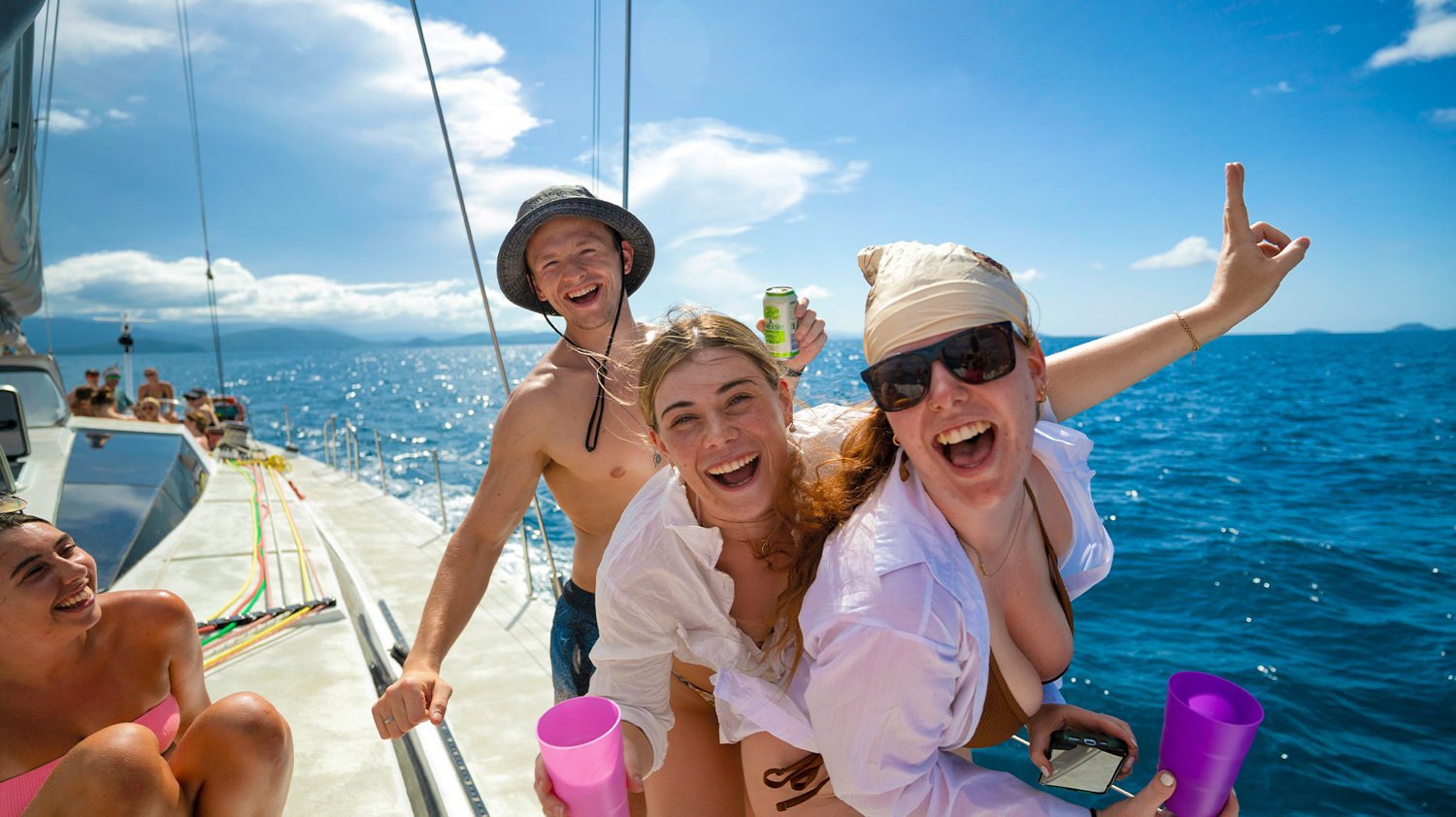 Three joyful backpackers laughing and having fun on a sailing boat in the Whitsundays.