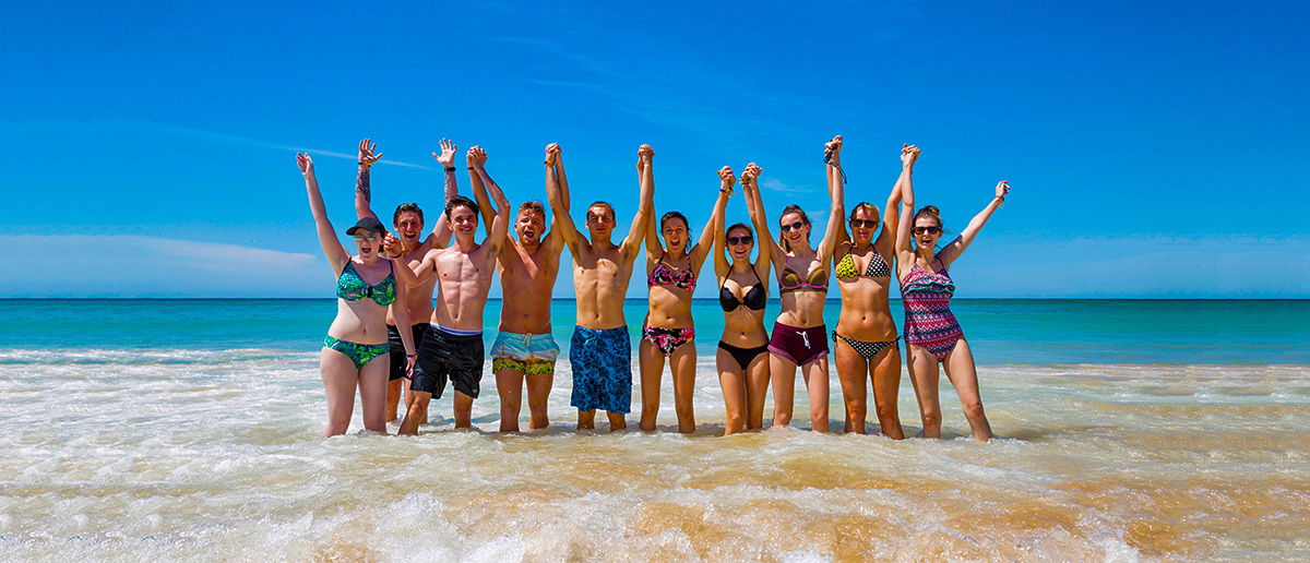 A happy group of young travelers raising their arms in the clear blue water at Bondi Beach.