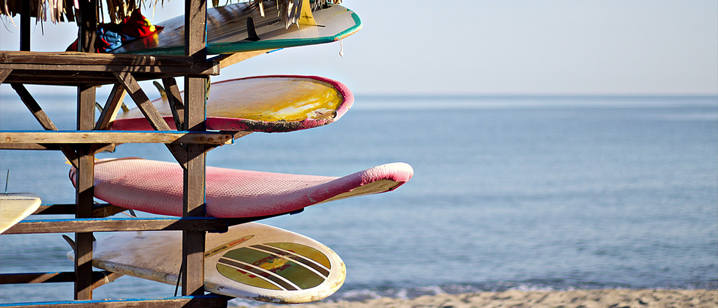 Colorful surfboards stacked on a wooden rack on the sandy beach at Byron Bay, Australia, with the ocean in the background.