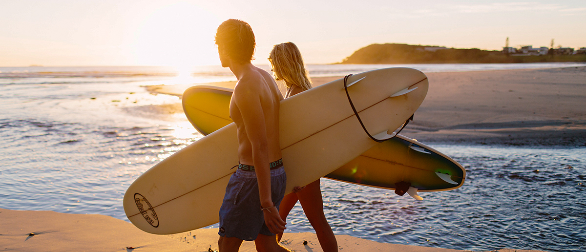 Two surfers walk along the beach with their boards at sunset in Byron Bay, Australia.