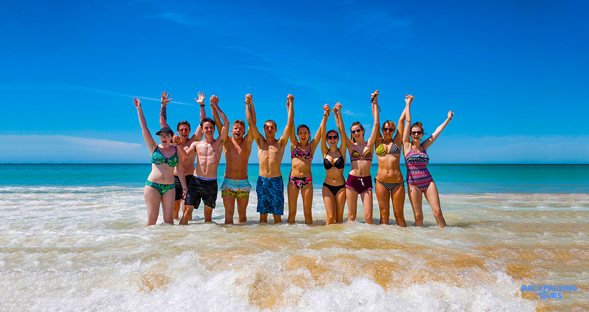 A joyful group of friends with raised arms celebrates in the clear ocean water at Bondi Beach.