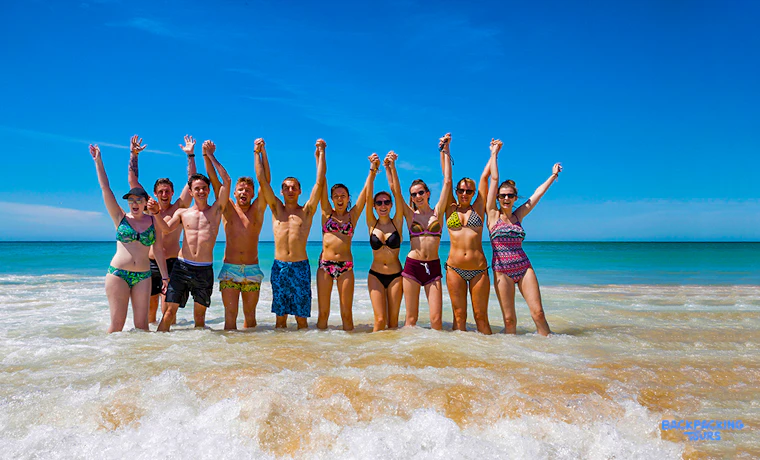 A joyful group of friends with raised arms celebrates in the clear ocean water at Bondi Beach.