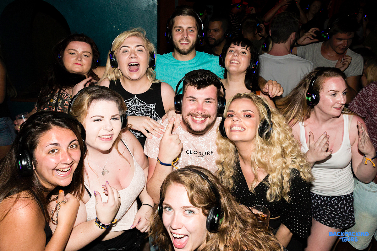 Smiling backpackers wearing headphones at a lively silent disco in Sydney, celebrating their first night.
