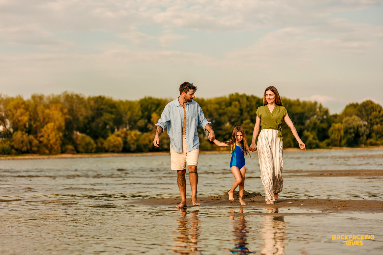 A happy family walks hand-in-hand along a shallow Seminyak beach at sunset, enjoying their vacation.