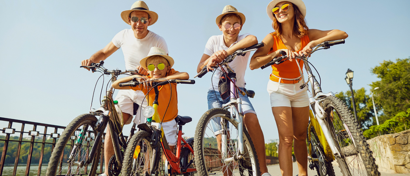 A happy family of four wearing hats and sunglasses, posing with their bicycles on Gili Trawangan.