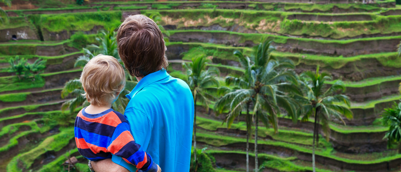 A man holds a child, looking out at the lush green terraced rice fields in Ubud, Bali.