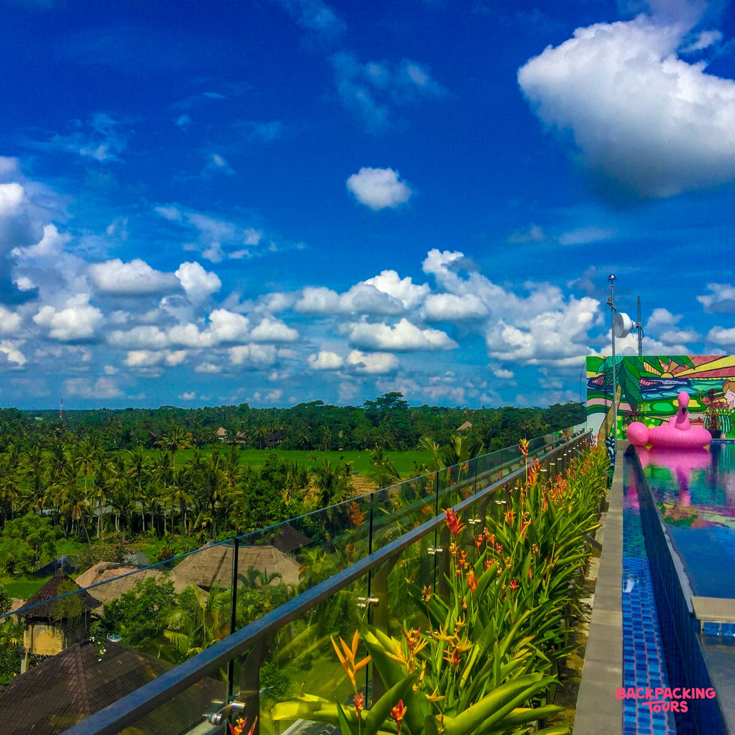 Stunning rooftop infinity pool with a pink flamingo float, overlooking lush green rice paddies in Ubud.
