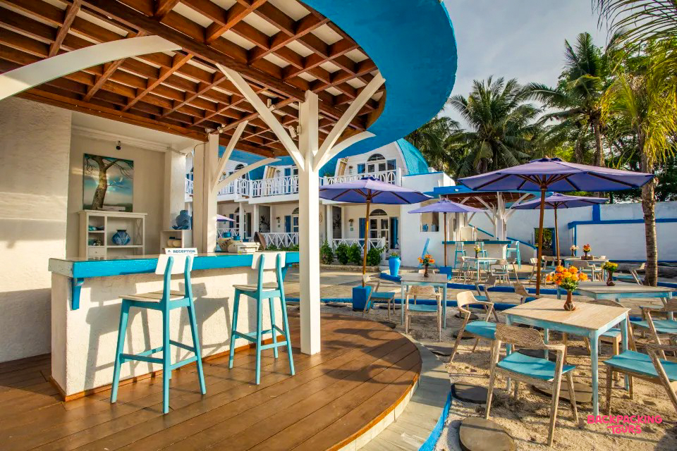 An inviting blue and white outdoor bar and restaurant with sand and palm trees on Gili Trawangan.