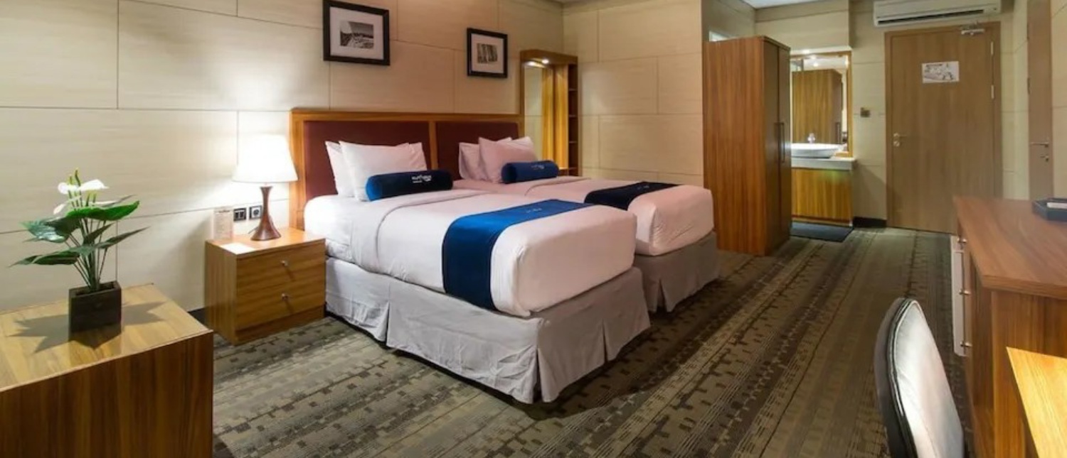 A clean and comfortable hotel room in Kuta, Bali, with two single beds and a bathroom entrance.