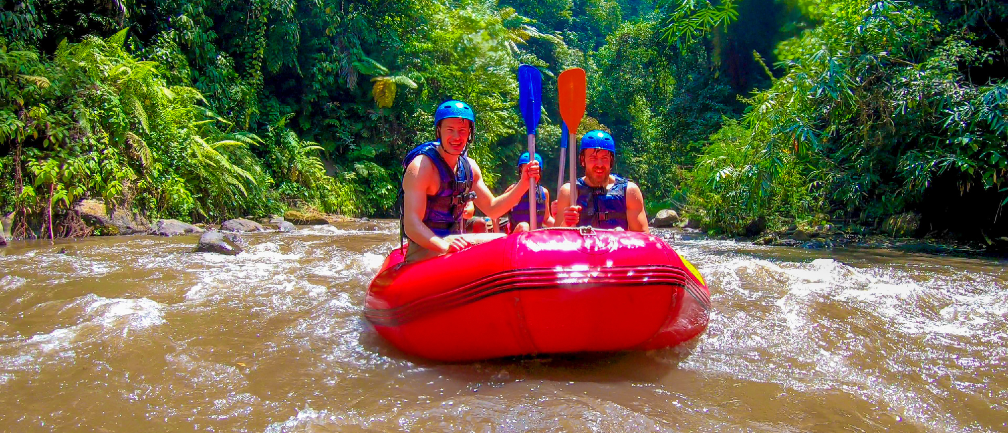 Two happy men rafting down a river through dense jungle in Ubud, Bali.