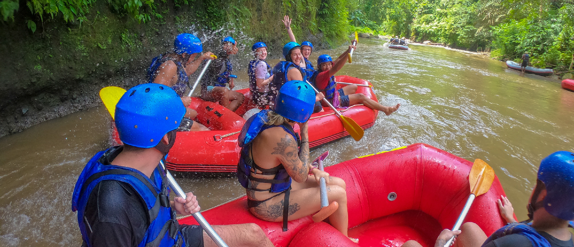 Happy rafters in red boats navigate a splashing river through the dense jungle in Ubud.