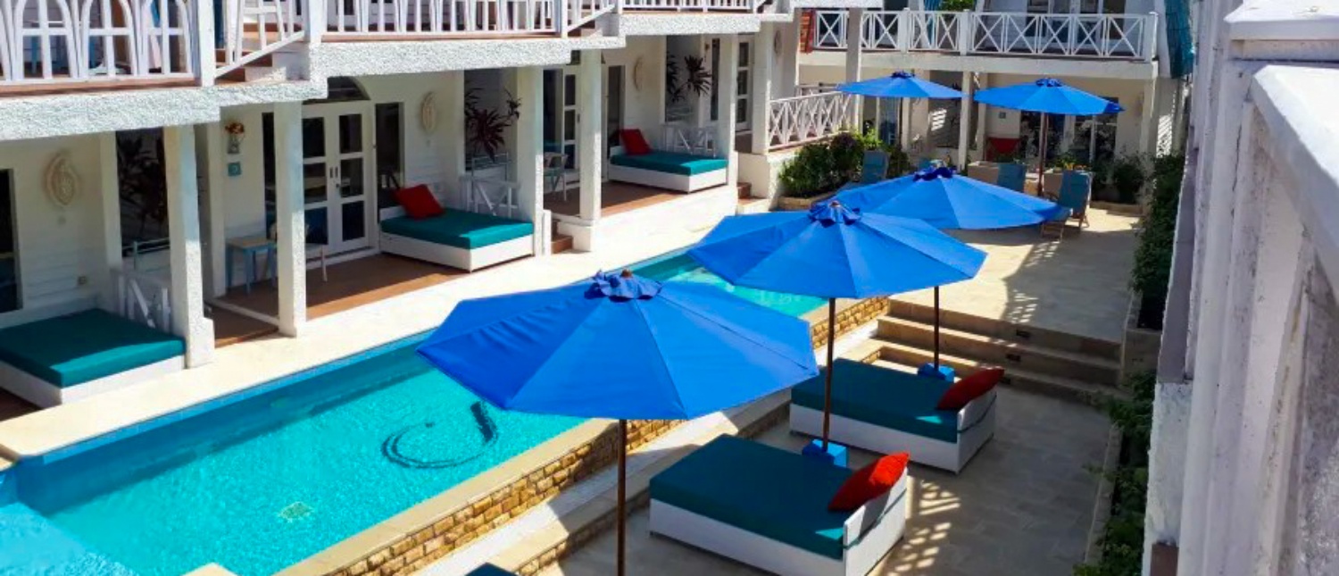 A bright resort courtyard on Gili Trawangan with a swimming pool, blue umbrellas, and sun loungers.