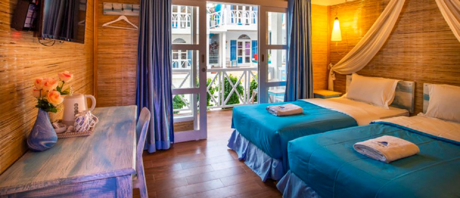 A bright hotel room in Gili Trawangan with two beds, blue accents, and a balcony view.