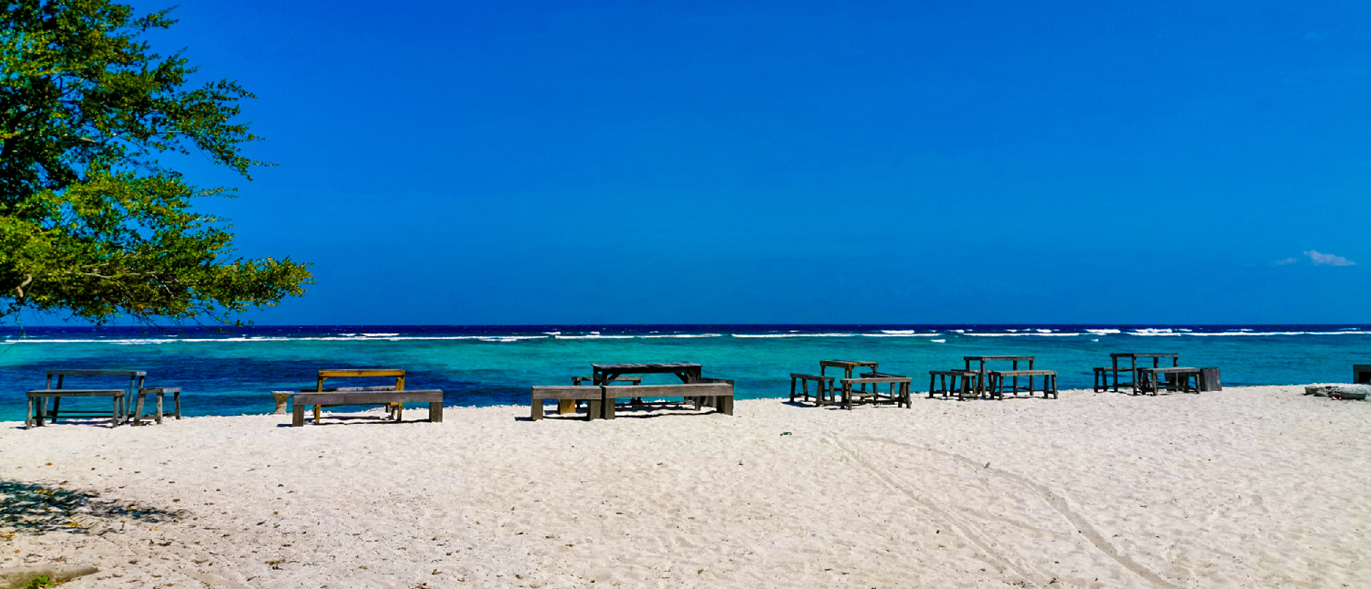 White sand beach with wooden tables, turquoise ocean, and clear blue sky on Gili Trawangan.