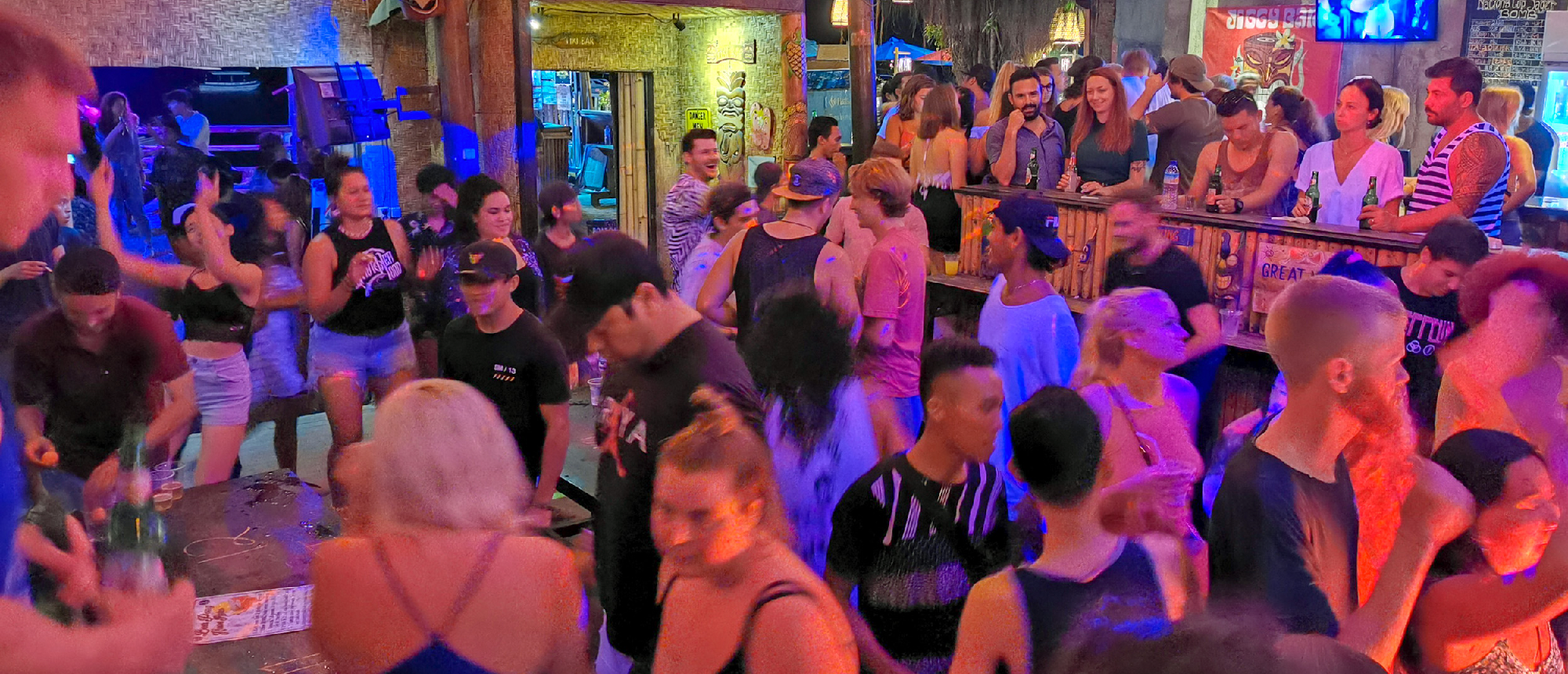Lively crowd of young people dancing and socializing at a vibrant Gili Trawangan bar at night.