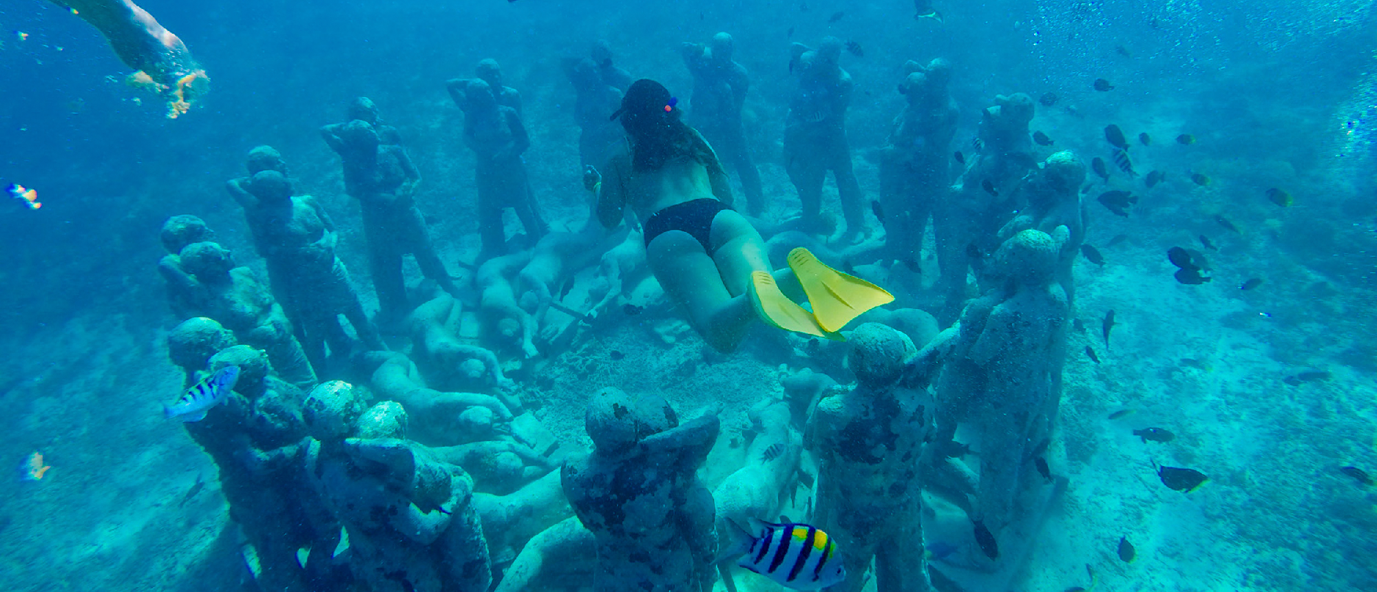 A snorkeler swims gracefully among an array of underwater statues in the clear blue waters of Gili Trawangan.