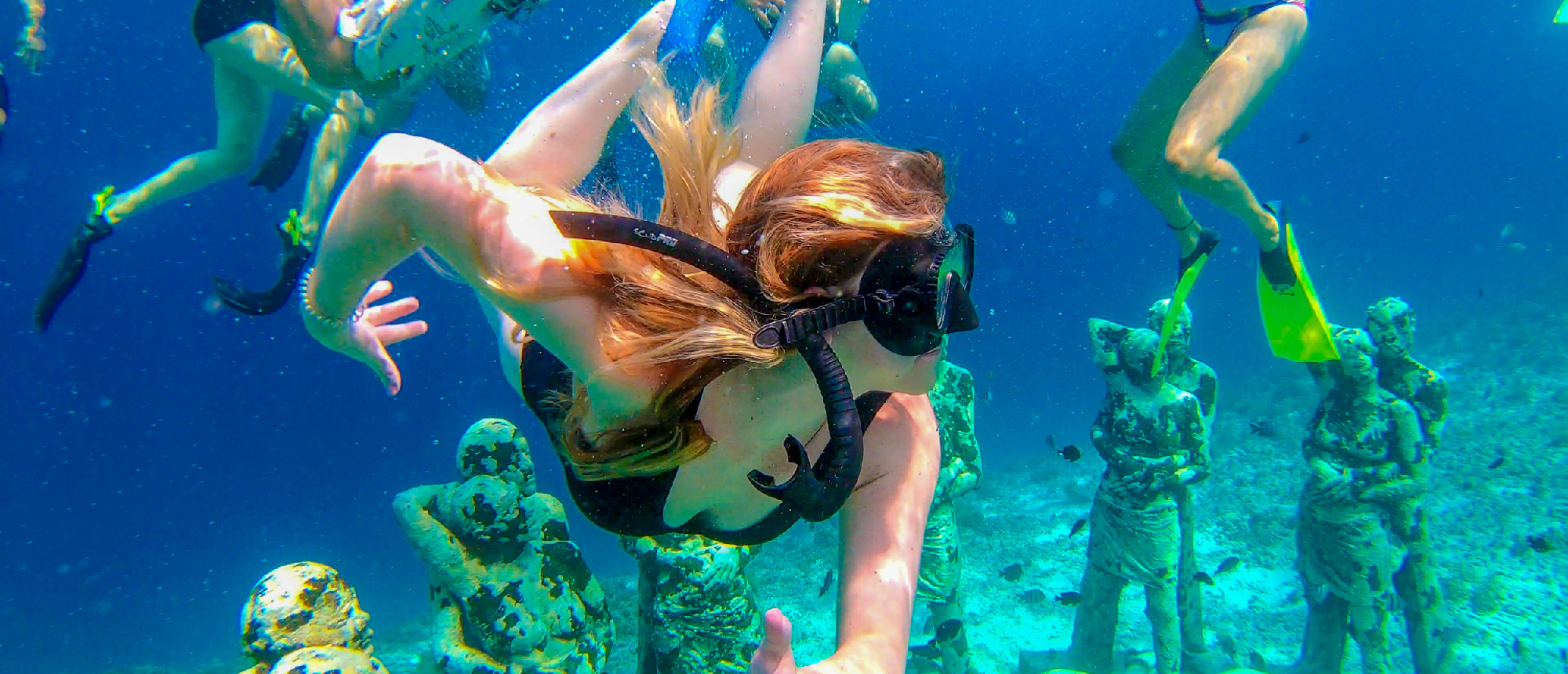 A woman with a snorkel mask swims gracefully among the serene underwater statues at Gili Trawangan.