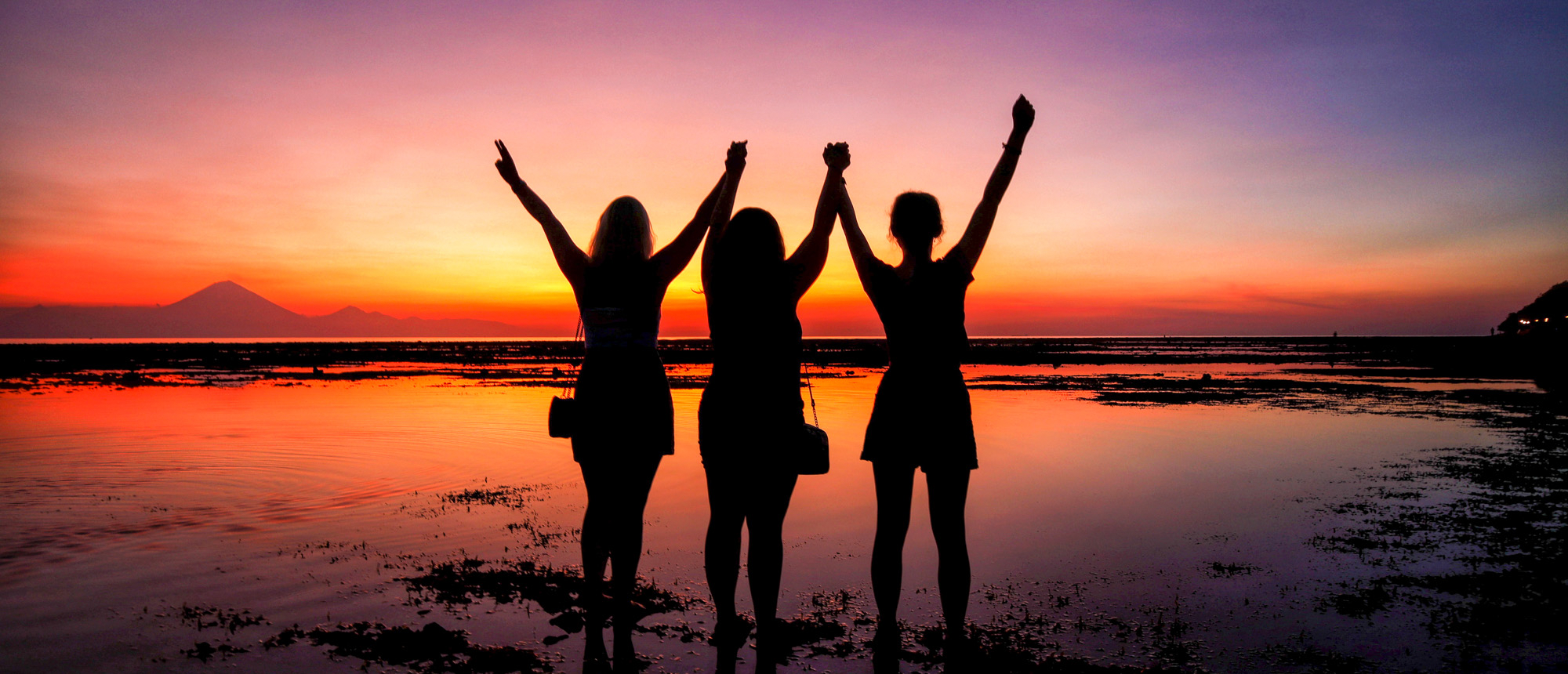 Three friends celebrate a stunning sunset on the beach in Gili Trawangan, Bali.
