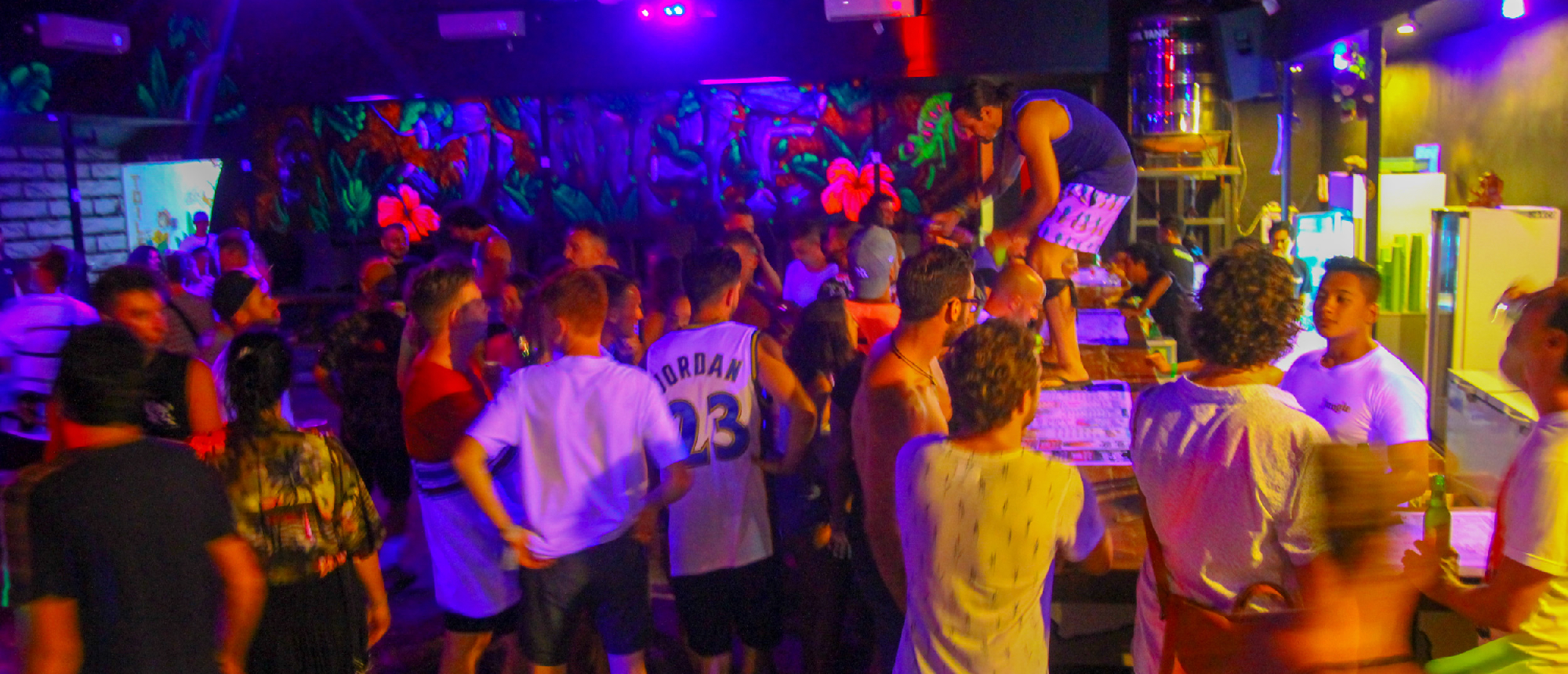 A lively crowd dances in a neon-lit bar on Gili Trawangan, with one person on the counter.
