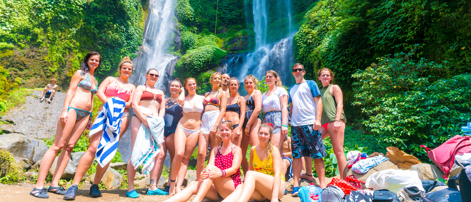A cheerful group of friends in swimsuits posing at the powerful Sekumpul Waterfall in Bali.