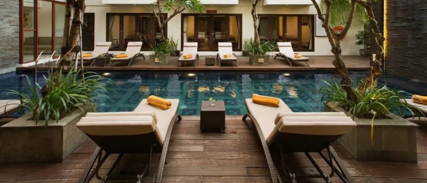 Relaxing hotel swimming pool with sun loungers and lush greenery in Seminyak, Bali.