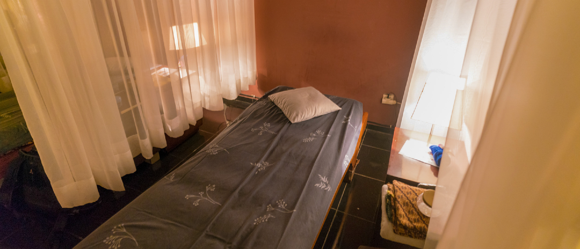 A tranquil spa treatment room with a massage bed, soft lighting, and flowing white curtains.