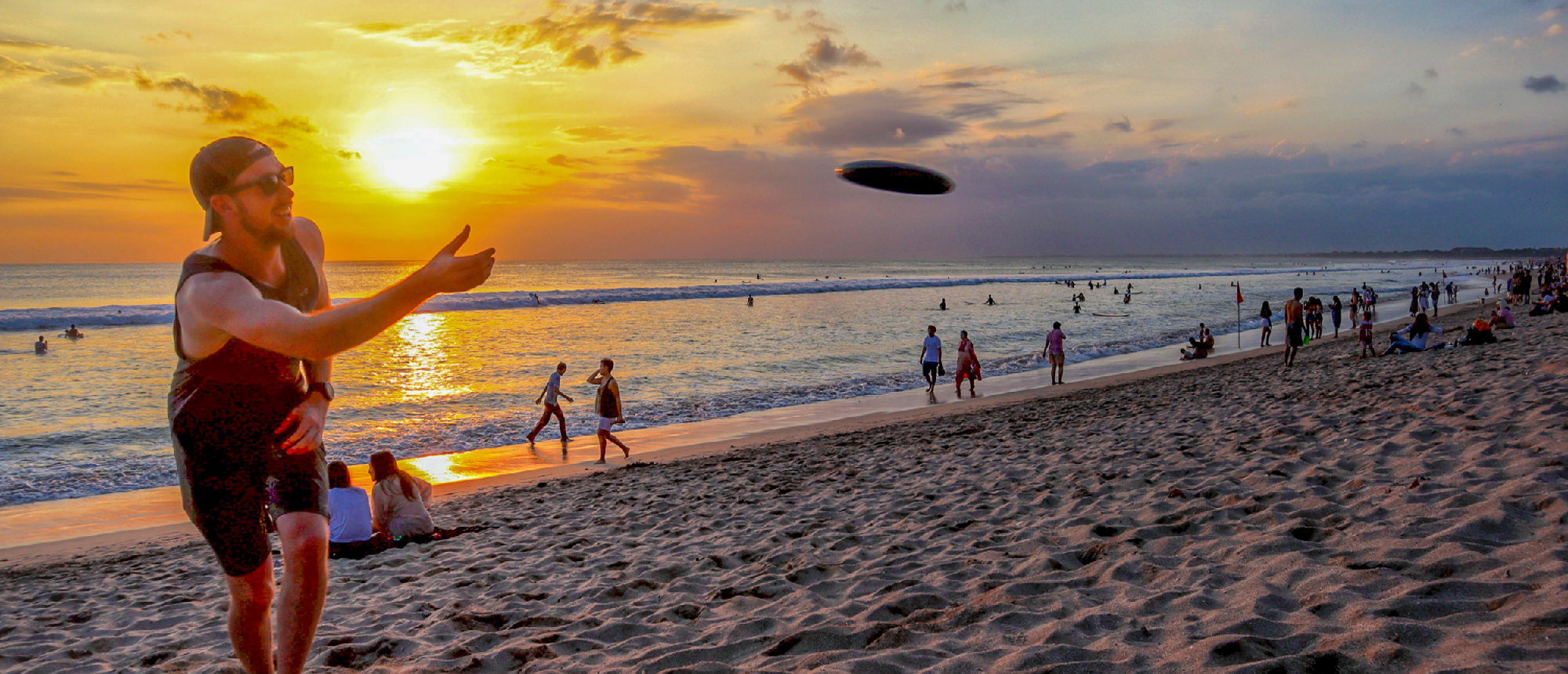 A man throws a frisbee on Kuta Beach in Bali during a beautiful sunset.