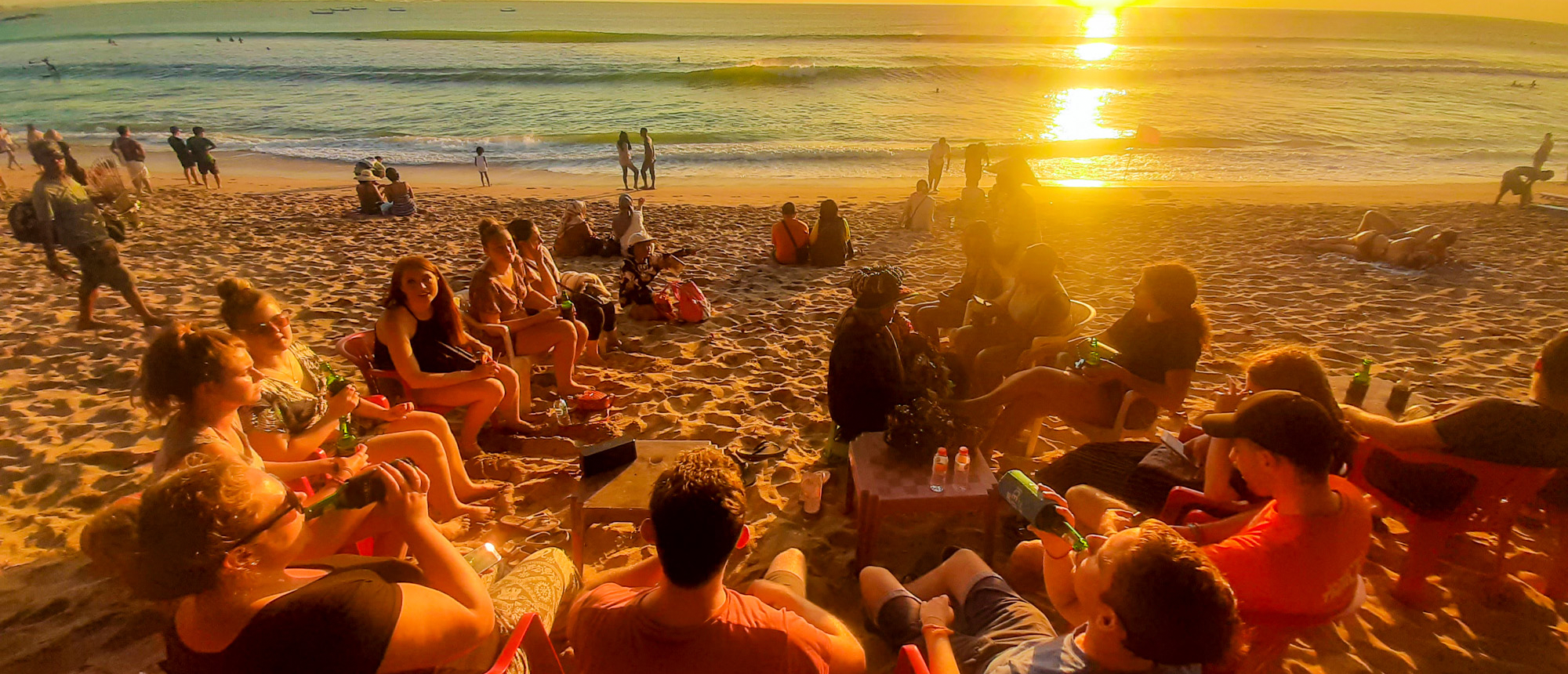 Backpackers relax on Kuta beach, enjoying drinks and a beautiful sunset over the ocean.