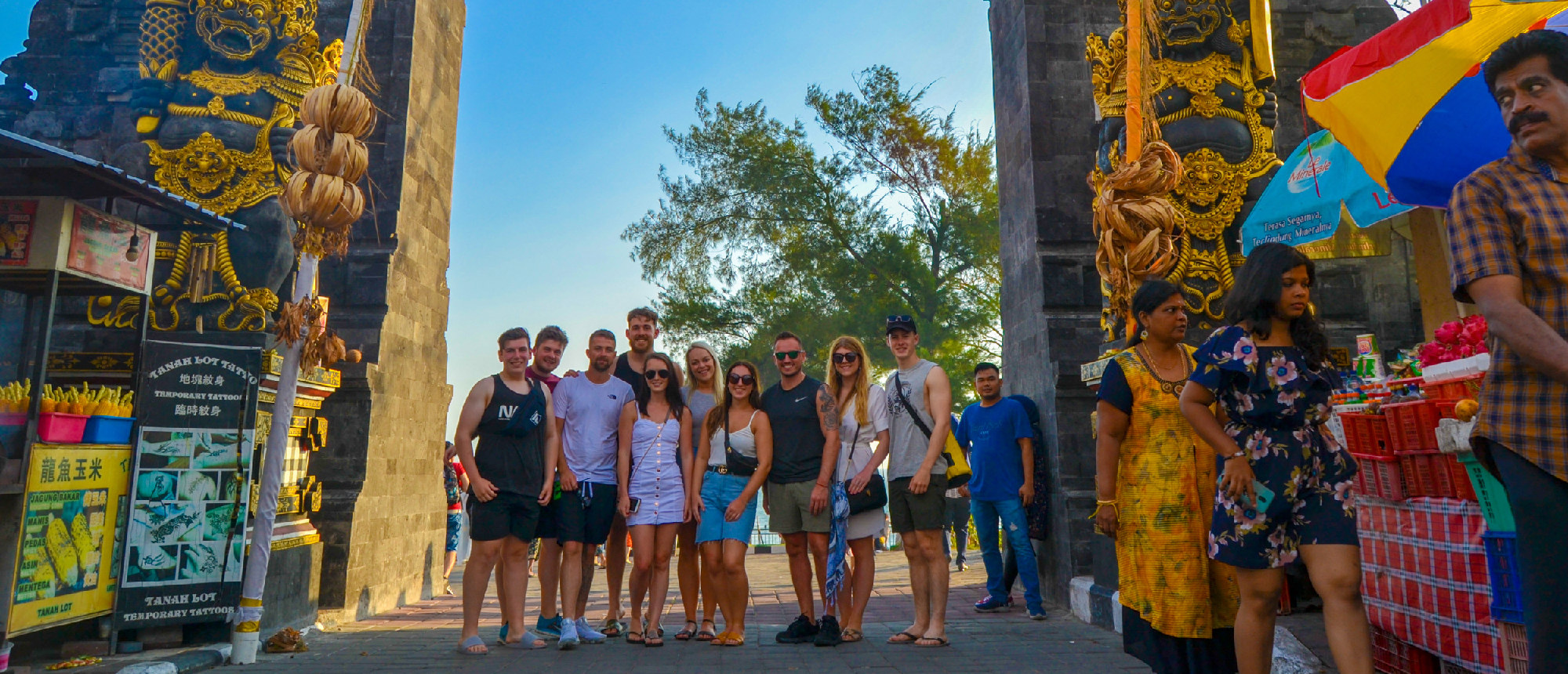 A happy group of young backpackers standing in front of an ornate Balinese temple gate in Kuta.