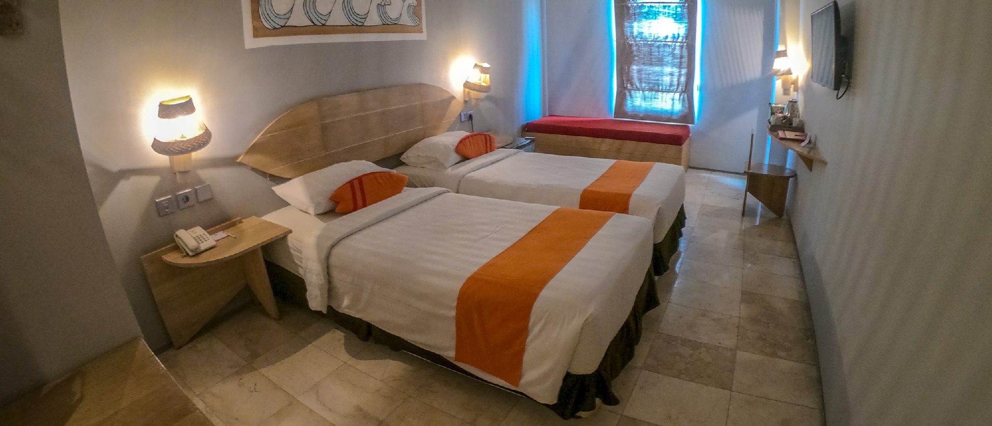 A bright hotel room in Kuta, Bali, with two twin beds, orange accents, and a window bench.