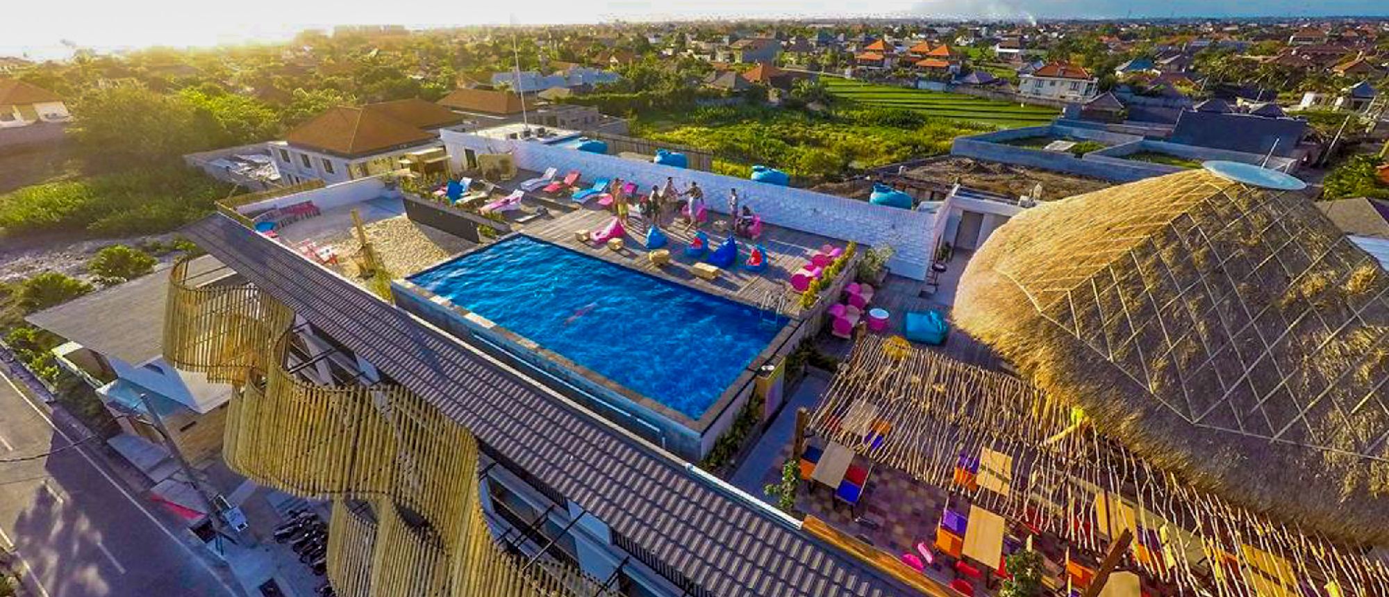 Aerial view of a vibrant rooftop pool and lounge with colorful bean bags in Kuta, Bali.