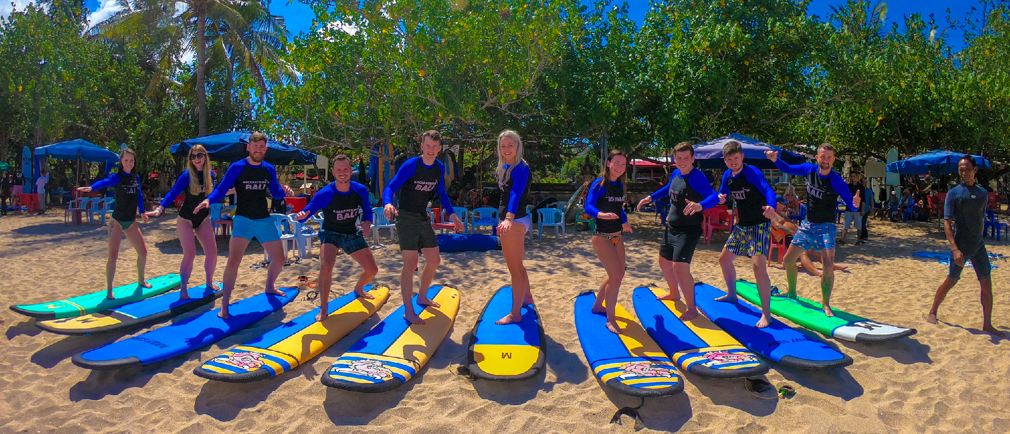 A group of happy backpackers practicing surfing stances on boards on a sunny beach in Kuta, Bali.